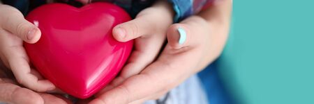 Close-up of kid and adult hands holding red plastic heart. Mum and child spending time together. Mothers day celebration. Symbol of love and relationshipの写真素材