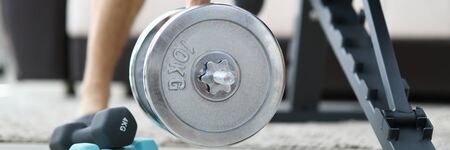 Male hand hold big silver dumbbell against house background closeup. Fitness training on self...