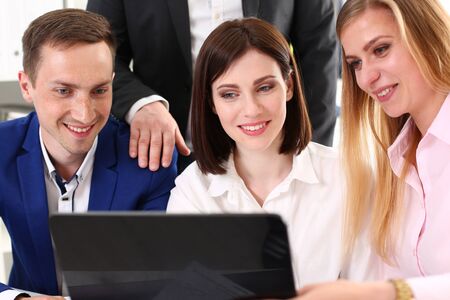 Group of young businesspeople looking at electronic pad PC and smiling while sitting at the table at...