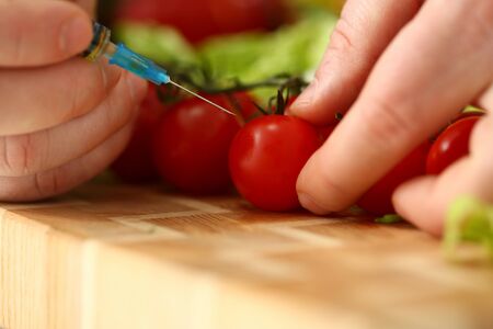 Close up of young man holding syringe and making injection to red ripe tomato