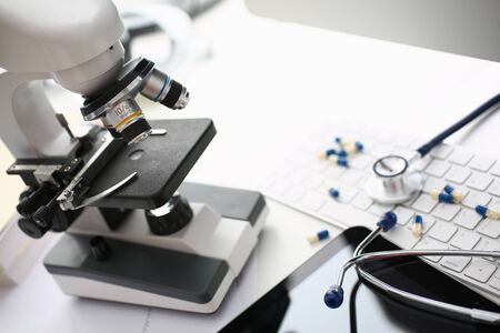 Close up of white table with laboratory optical microscope, pharmaceutical drugs, keyboard and...