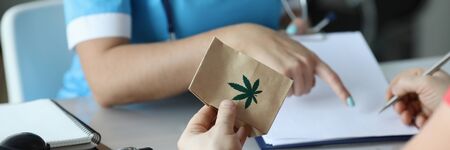 Close-up of patient holding package with cannabis and leaf sign. Signing document. Stethoscope on office desk. Doctors appointment and traditional medicine conceptの写真素材