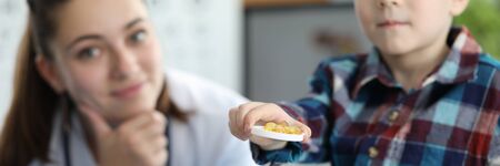 Close-up of little boy holding golden capsules in container. Smiling young pediatrician with stethoscope on neck. Planned checkup and modern medicine conceptの写真素材