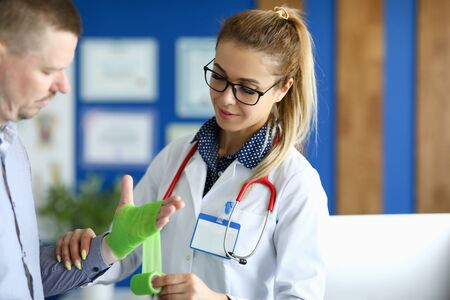 Portrait of surgeon making bandaging of hand with elastic bandage. Male person examining by doctor. Nurse in medical uniform. Healthcare and prevention conceptの写真素材