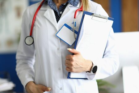 Close-up of doctor holding paper folder with patient form. Practitioner working in hospital. Person with stethoscope and badge. Healthcare and prevention conceptの写真素材