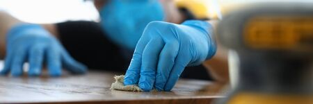 Carpenter in gloves cleans polishes wooden surface. Joiner polish wooden surface canvas on table....