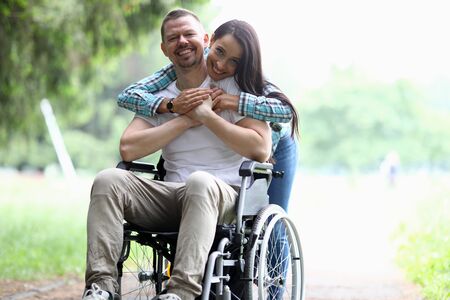 Portrait of happy sweet couple spending time together in nature. Attractive woman embrace man and smiling on camera. Cheerful people in park. Happiness and disabled people conceptの写真素材