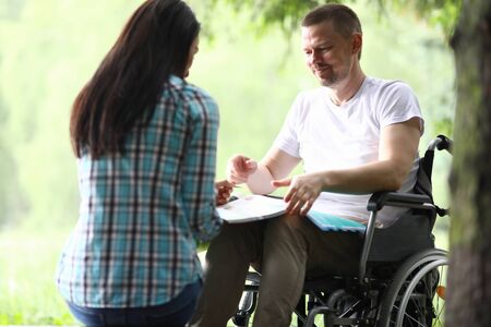 Portrait of smiling man sitting in wheelchair with papers. Handsome middle aged person in white...