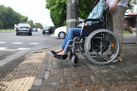 Close-up of man accompany female in wheelchair. Person taking care of lover. Carefully crossing street. Lady in jeans and blue shirt. Walk in city. Disabled people conceptの写真素材