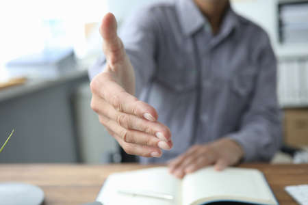 Cropped photo of young confident businessman giving an handshake while sitting at desk. Recruitment conceptの写真素材
