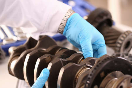Close up of mechanic wearing protective gloves and repairing a crankshaft from a car