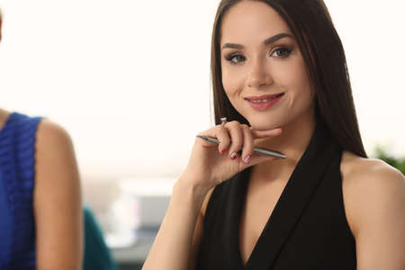 Smiling brunette attractive lady holding pen and looking at camera during business meetingの写真素材