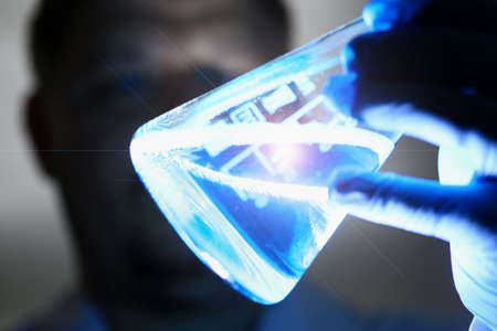 Close up of male researcher using and looking at test tube of clear solution in laboratory. Chemistry and biology conceptの写真素材