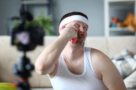 Handsome brunette funny man fooling around with dumbbells while posing on camera and shooting vlog...