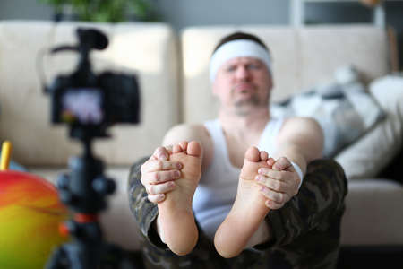 Concentrated adult man doing exercise while shooting video content for his blog at home. Health and...