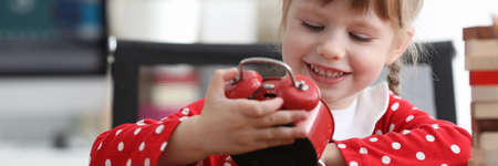 Little cute girl looks at alarm clock and laughs. Cute games for girls to show imagination....