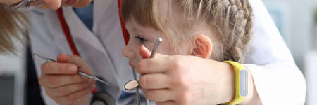 Pediatric dentist examines teeth little girl. Examination oral cavity in children at various age periods. Identification pathological conditions teeth in girl. Diseases development in childrenの写真素材