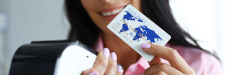 Happy girl holds credit card and terminal for use. Bank employee explains how to pay by credit card through wireless terminal. Increasing customer loyalty and increasing average checkの写真素材