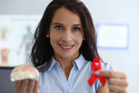 Happy woman shows breast implant and red ribbon. Way out critical situation an oncologically ill...