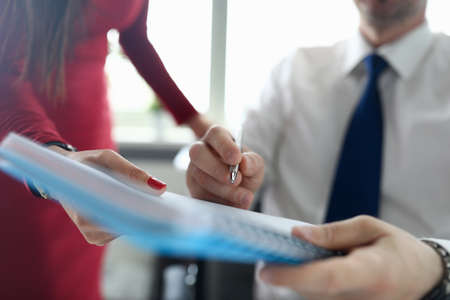 Close-up of female secretary giving paper for signing to male boss. Man in suit holding silver pen. Stylish costume. Good deal. Successful business and career growth conceptの写真素材