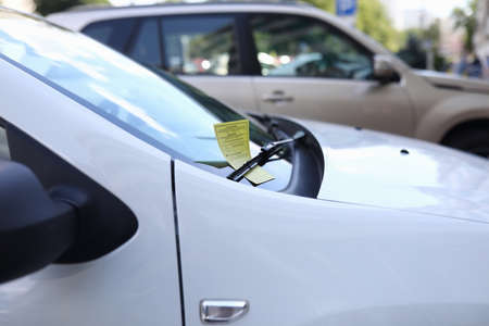Close-up of white automobile with parking ticket under windshield wiper. Auto on street. Penalty...
