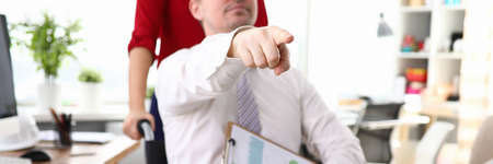 Close-up of male in wheelchair pointing with finger where wants to go. Worker holding clipboard with...