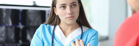 Close-up of serious doctor listening to patient. Young concentrated female wearing uniform and professional equipment stethoscope. Modern medicine and x ray conceptの写真素材
