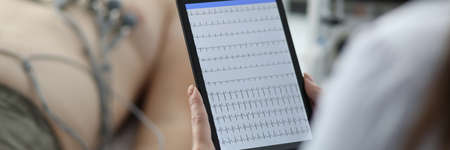 Close-up of female cardiologist holding tablet and examine patients heartbeat. Person laying on hospital bed with special equipment on chest. Medicine and cardiology conceptの写真素材