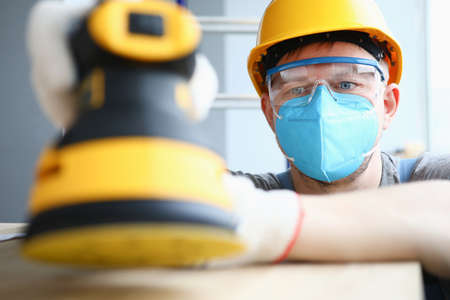 A carpenter in gloves holds a grinding machine. Preliminary cleaning and polishing of surfacesの写真素材