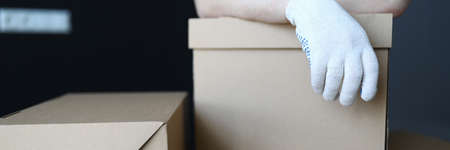 Gloved hands loader lie on cardboard boxes office. Relocation service packed property in separate boxes. Packaging signed. Employee ensures their safety. Work is performed by qualified specialistの写真素材