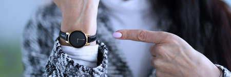 Displeased woman shows time on her wristwatch. Woman analyzes market in global and local senses, calculating possible risks. Process implementing decisions and monitoring their implementationの写真素材