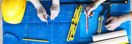 Top view of two architects painting project of house. Professional master-builder using pencil and...