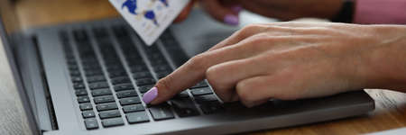 Close-up of female hand typing text on laptop. Businesswoman paying for service of product in...