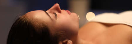 Close-up of relaxed young woman laying on table in spa center. Relaxing massage and body care procedure. Soft lights and comfort for client. Wellness health and beauty conceptの写真素材