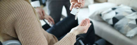 Close-up of male businessman giving keys from new house to disabled woman. Female sitting in...