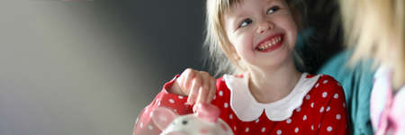 Happy little girl in red dress hold silver coin in hand. Home finance budget concept