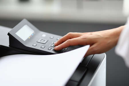 A woman uses office equipment to print. Hand presses buttons on printer. Cost-effective and easy device managementの写真素材