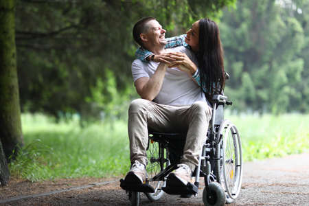 Happy young couple walks in the park. Woman hugs a guy sitting on a wheelchairの写真素材