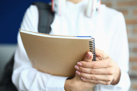 A student with a backpack holds notebooks for study. Young trainee in business clothes with headphones on his neckの写真素材
