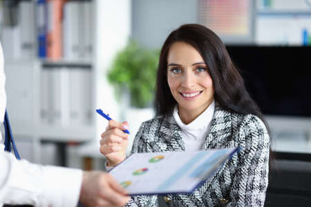Beautiful woman manager holds a pen for signing a document. A man sits in front of a woman with a report in his handsの写真素材