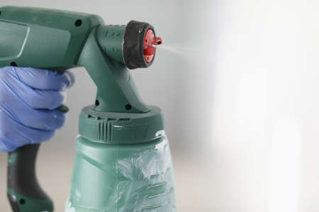 A hand in a glove holds special equipment for spraying paint close-up. Repairing the building from the insideの写真素材