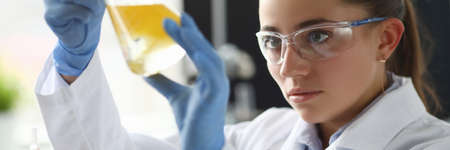 Chemist girl looks at flask with yellow liquid. Experiments and research pharmacist. Laboratory...