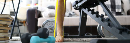 Close-up of man training at home using yellow rubber band for leg exercise. Strong and fit body on quarantine period. Necessary equipment indoors. Sport and active lifestyle conceptの写真素材