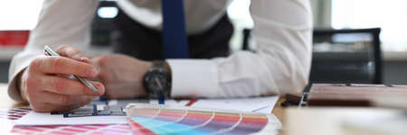 Close-up of man in stylish suit holding silver pen. Male person in office. Creative designer and architect. Colourful samples palette. House renovation and new interior conceptの写真素材