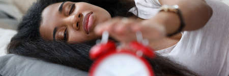 Portrait of sleepy brunette lying on comfortable bed. Awake lady turning off alarm clock. Morning...