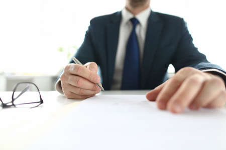 Businessman sits at table holding a pen over document. Business and Political Agreements Conceptの写真素材