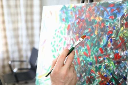 Artist hold brush in his hand. Close up male hand draw picture with multi-colored paint. Painting...