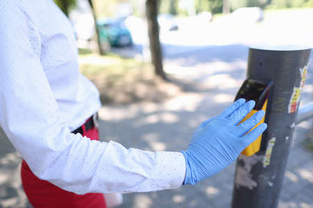 Woman in a glove at pedestrian crossing puts her hand to board to control pedestrian crossing. Health safety in public areas in coronavirusの写真素材