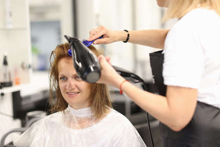 Hairdresser makes clients hair styled with hairdryer and comb. Hair styling training and courses conceptの写真素材