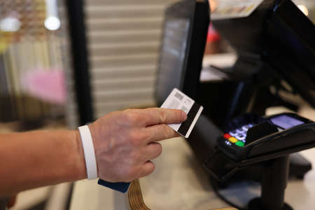 Mans hand holds a plastic card in his hands and applies it to terminal. Safe payments by bank cards...